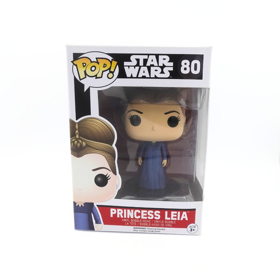 Front on photograph of the Princess Leia 80 Star Wars Funko Pop, with the figure itself visible through the plastic bubble. The cardboard depicts the number, franchise and illustration of Leia as well as the Pop! logo