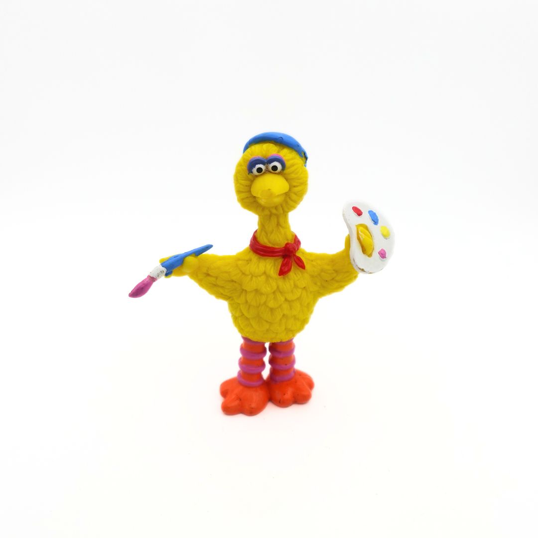 A yellow Big Bird figure holding a paint brush and paint palette while wearing a beret and scarf