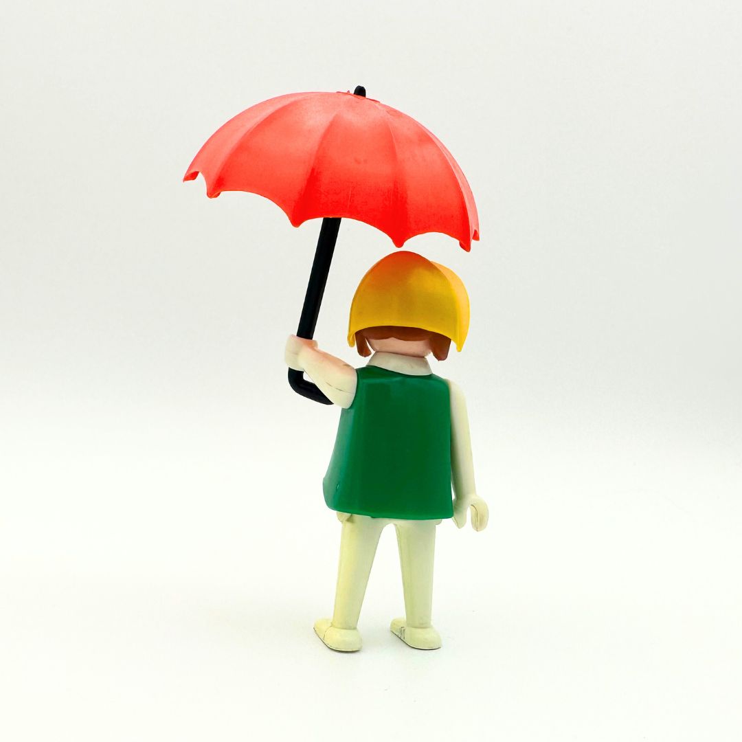 A 70s Geobra doll in great condition with a green shirt, white pants, a yellow hat and red umbrella