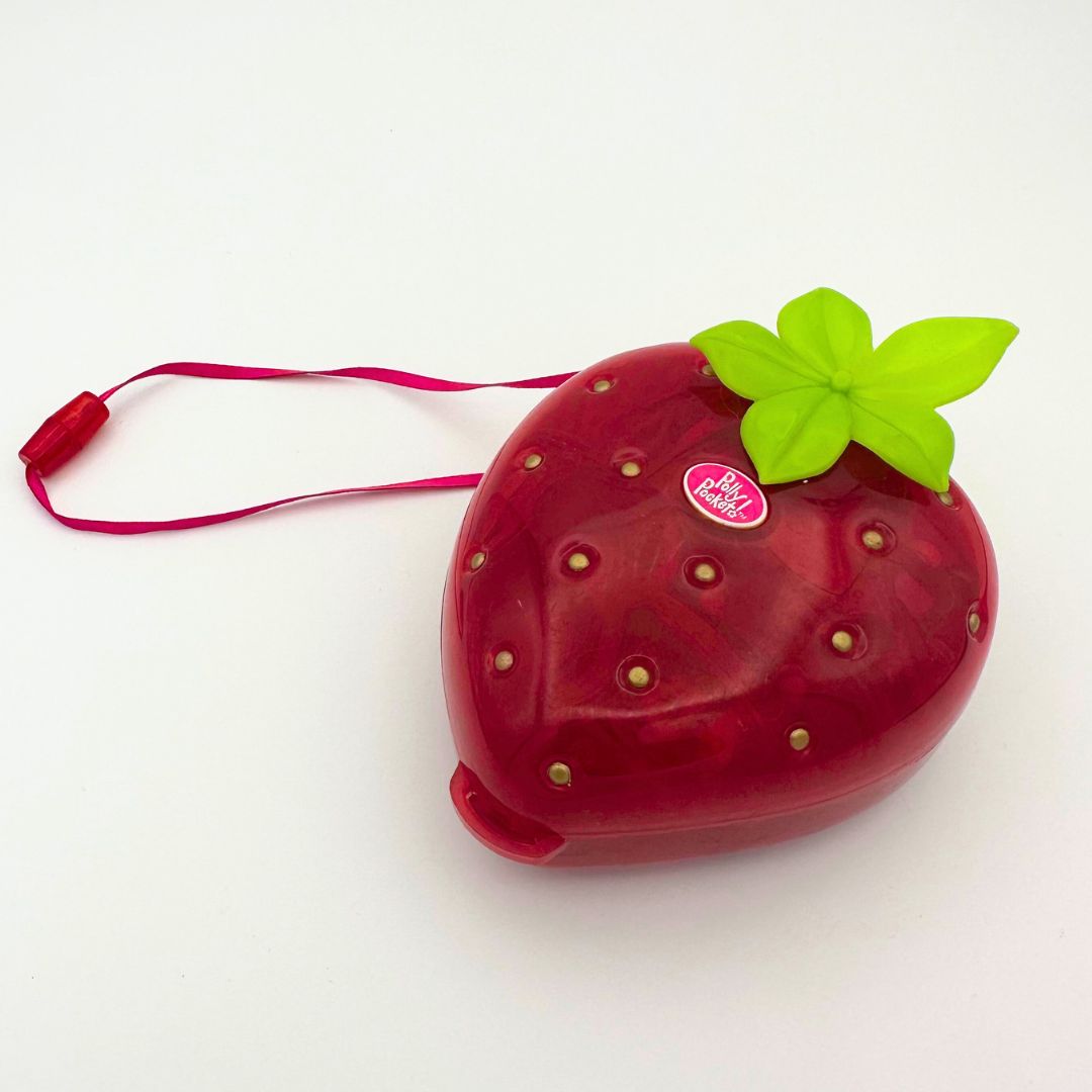 A photo of the closed Strawberry Polly Pocket from the nineties, featuring a carry ribbon
