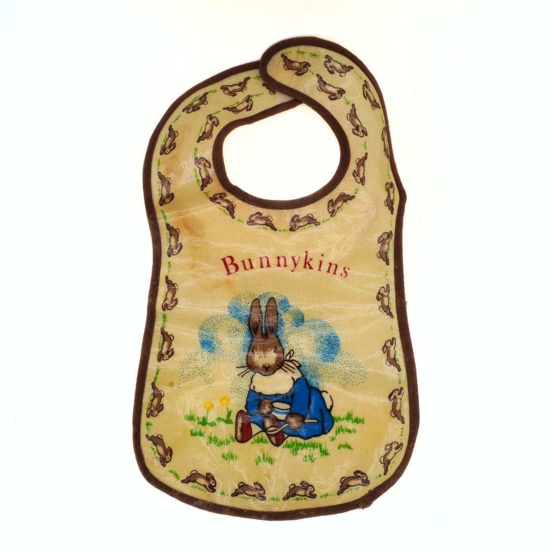 Baby bib with rabbit design and 'Bunnykins' text on a beige background