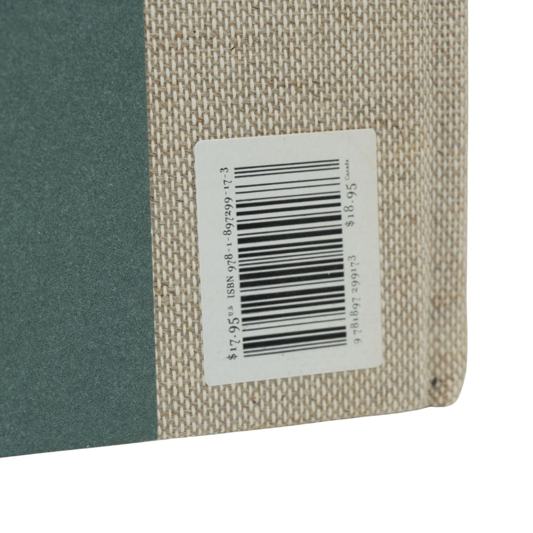 Close-up of the corner of a book showing a dark green cover on the left and a beige woven fabric binding on the right, with a white barcode label attached.