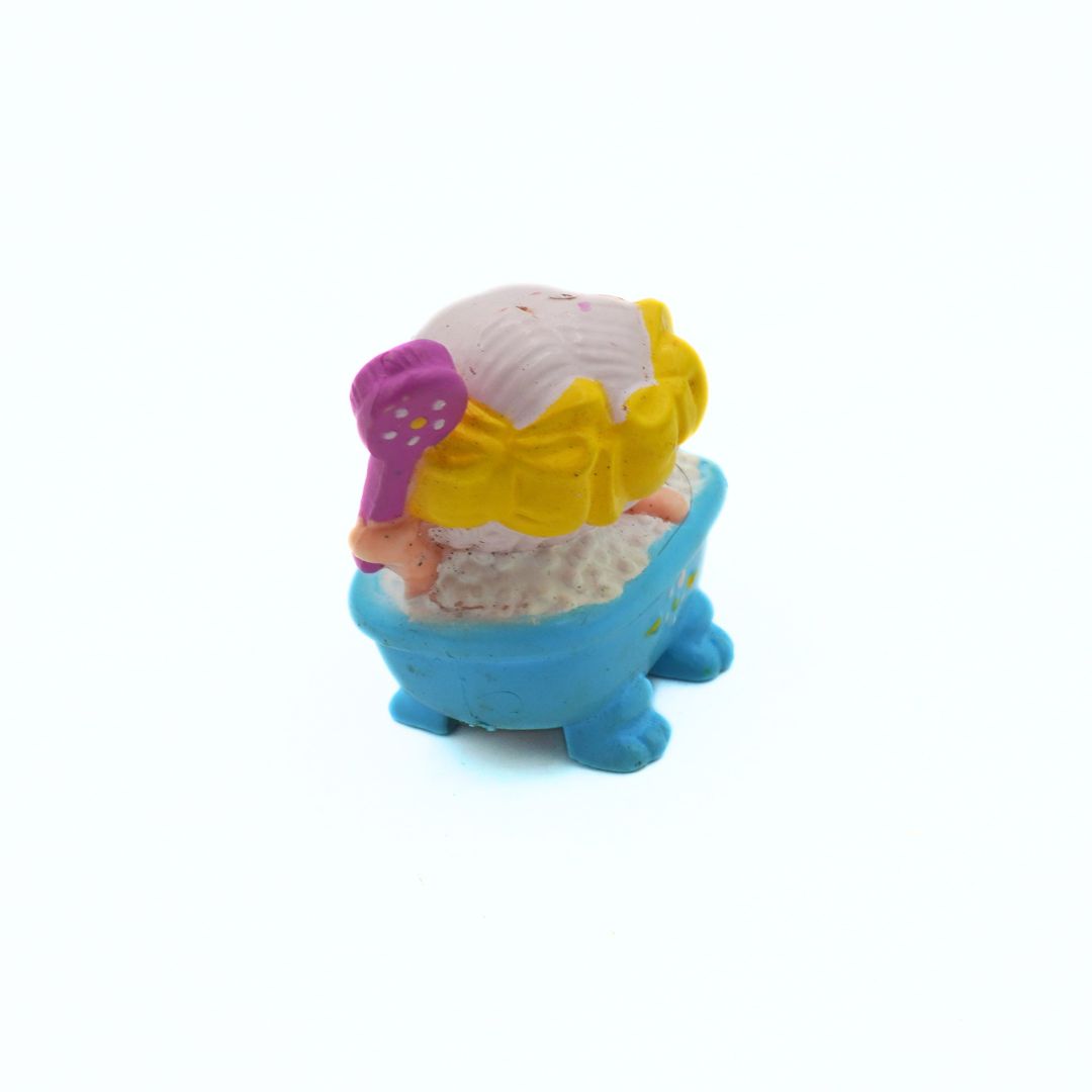 Toy figure of a character with a blue bath and pink and yellow accessories on a white background