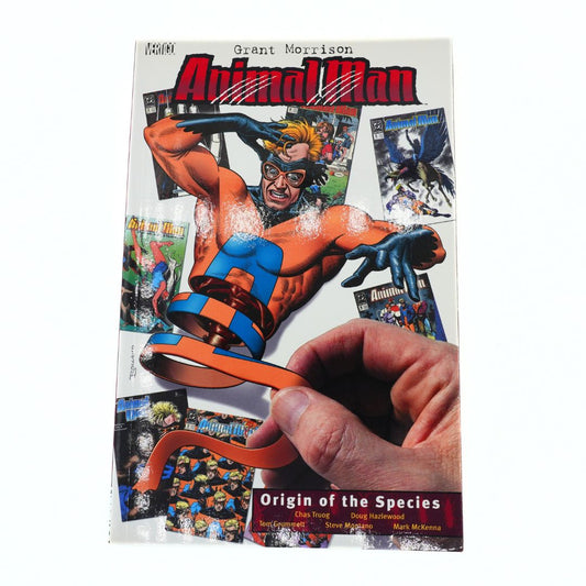 The front cover of the comic book 'Animal Man: Origin of the Species' by Grant Morrison, featuring a hand holding a large orange ribbon in front of the cover art, photographed on a white background.