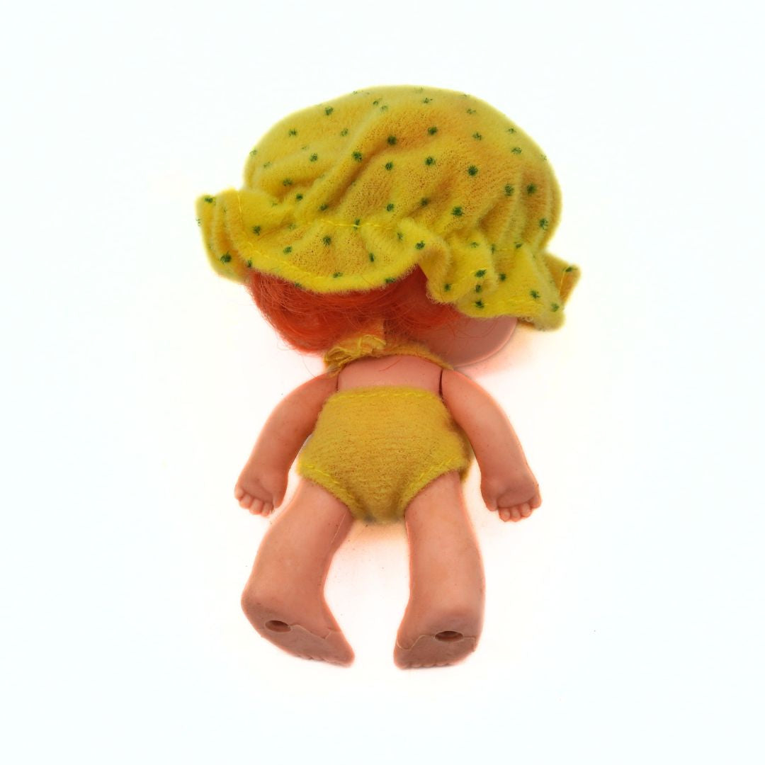Small doll wearing a yellow outfit and hat on a white background