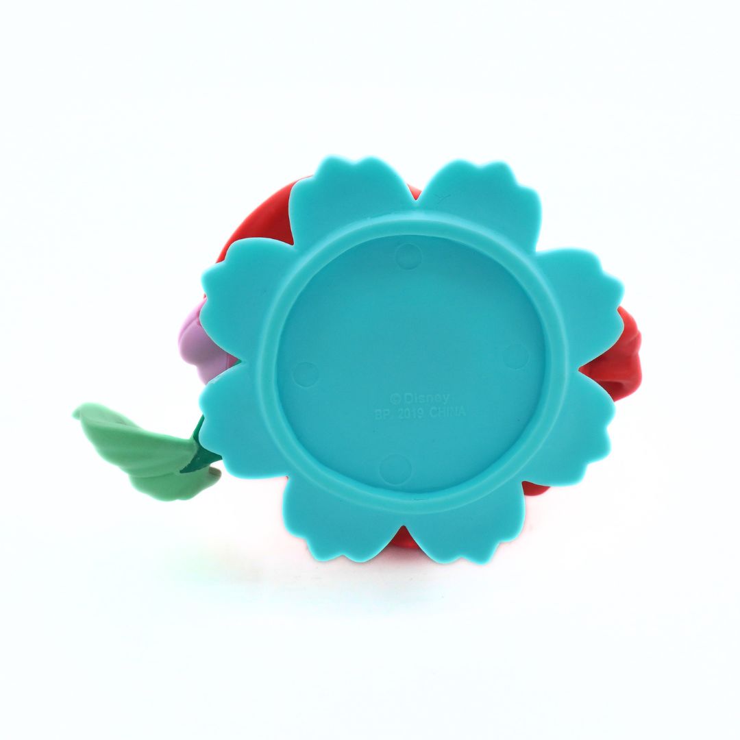 A close-up of a colorful plastic toy or accessory shown from the back, featuring a large turquoise flower-shaped top with scalloped edges, red sides, a small green leaf-like piece on the left, and a purple section behind it, photographed on a white background.
