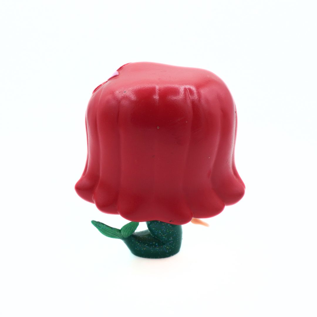 A small stylized figurine or toy with a large rounded red top resembling a flower or helmet-like shape, attached to a glittery dark green base with two green leaves, photographed on a plain white background.