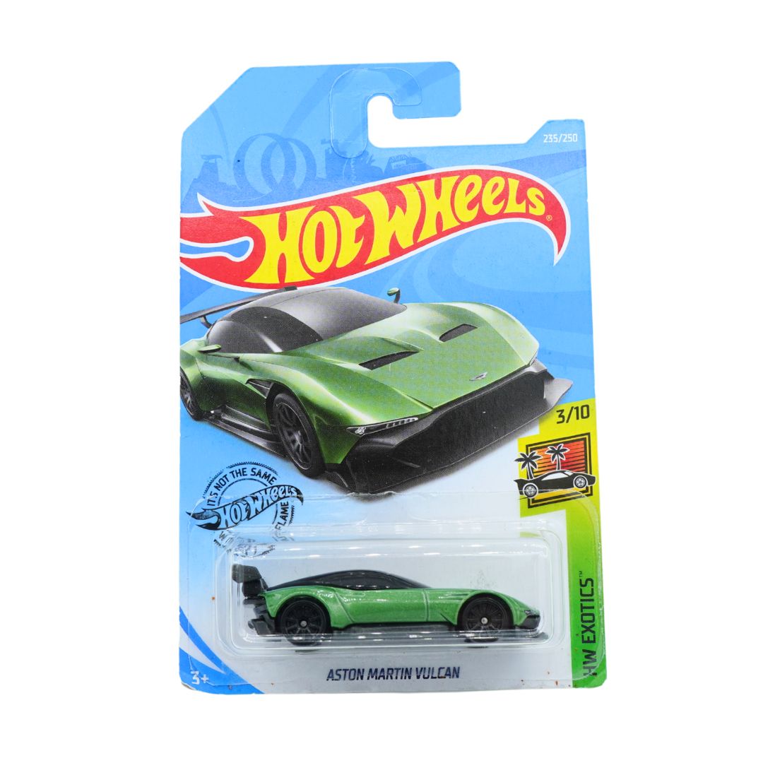 A Hot Wheels die-cast toy car of the Aston Martin Vulcan, shown in its original blister card packaging. The packaging features a blue background with the iconic red and yellow Hot Wheels logo, and a graphic of the green car.