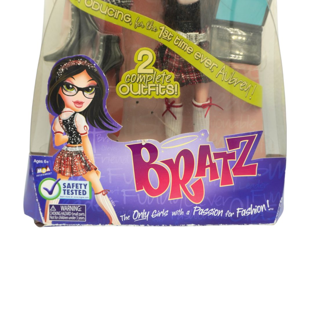 Bratz doll in its original retail packaging, featuring a character with long dark hair and glasses, dressed in a black and white outfit with red accents. The box displays the 'Bratz' logo and promotional text.