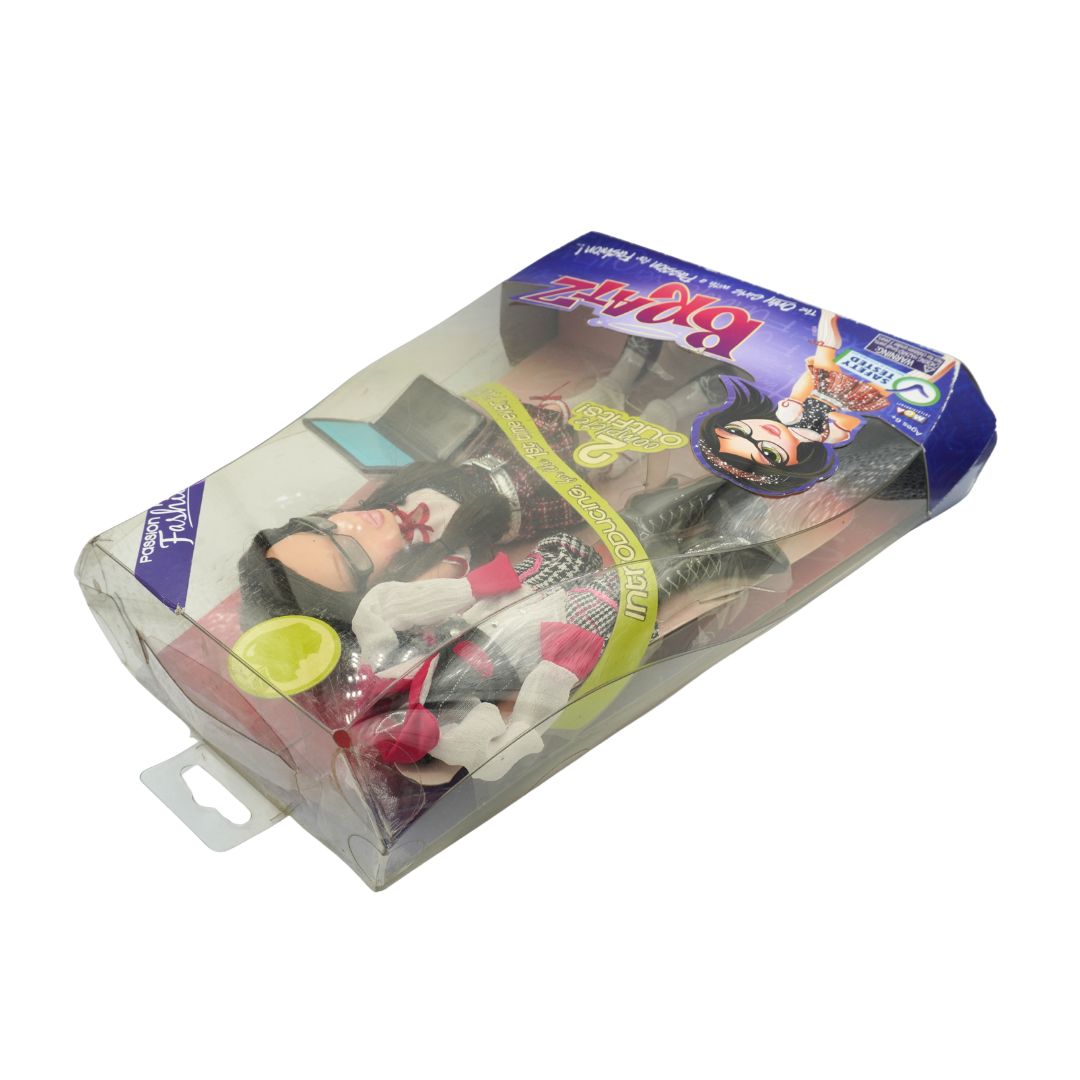 A packaged doll set in clear plastic blister packaging with a purple and blue cardboard header. The doll has dark hair, a black top, white gloves, and red-and-white striped bottoms, with a small yellow-green accessory visible.