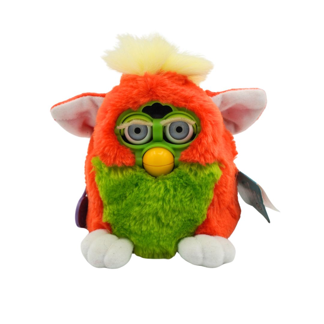 An orange and green Furby with yellow hair and blue eyes, photographed against a white background