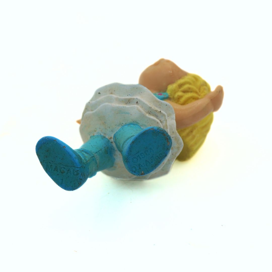 Small figurine of a person lying down with a blue object on a white background