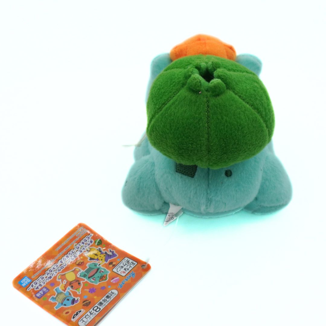 Plush toy resembling a green dinosaur with an orange hat next to a colorful card on a white background