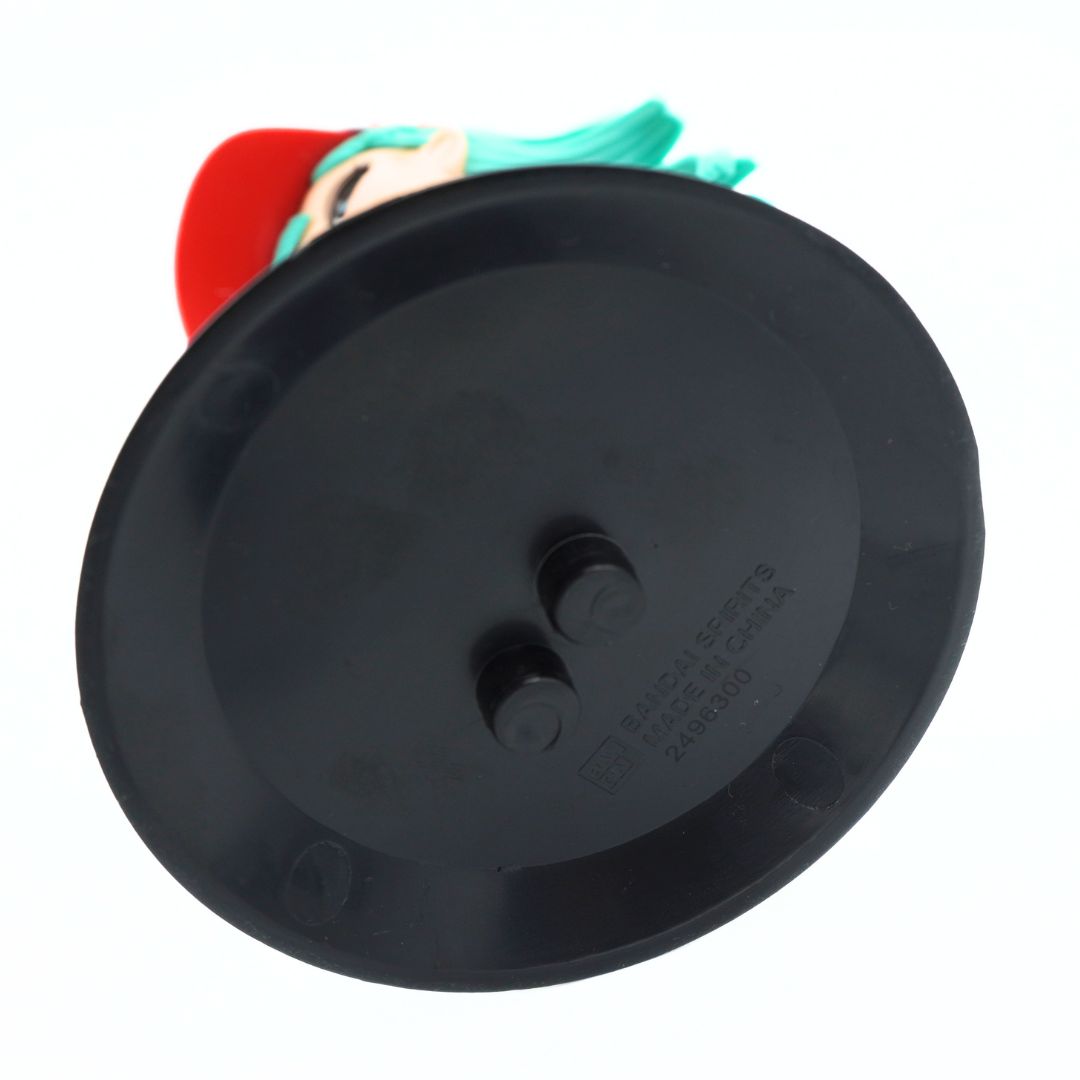 A close-up of a black plastic circular base or lid with two small protruding studs, showing part of a colorful object behind it on a white background.