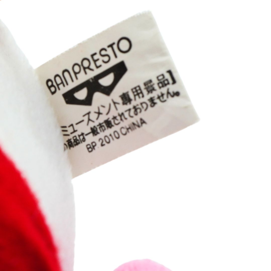 Close-up of a Banresto plush toy tag with Japanese text and a black mask logo, attached to a white and red plush fabric on a white background.