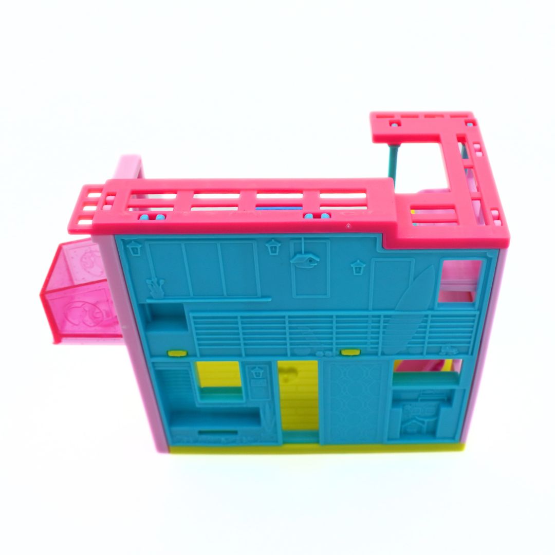 A colorful plastic toy building or dollhouse structure with a bright cyan main body, hot pink outer frame and attached translucent pink panel, plus small yellow details, photographed on a plain white background.