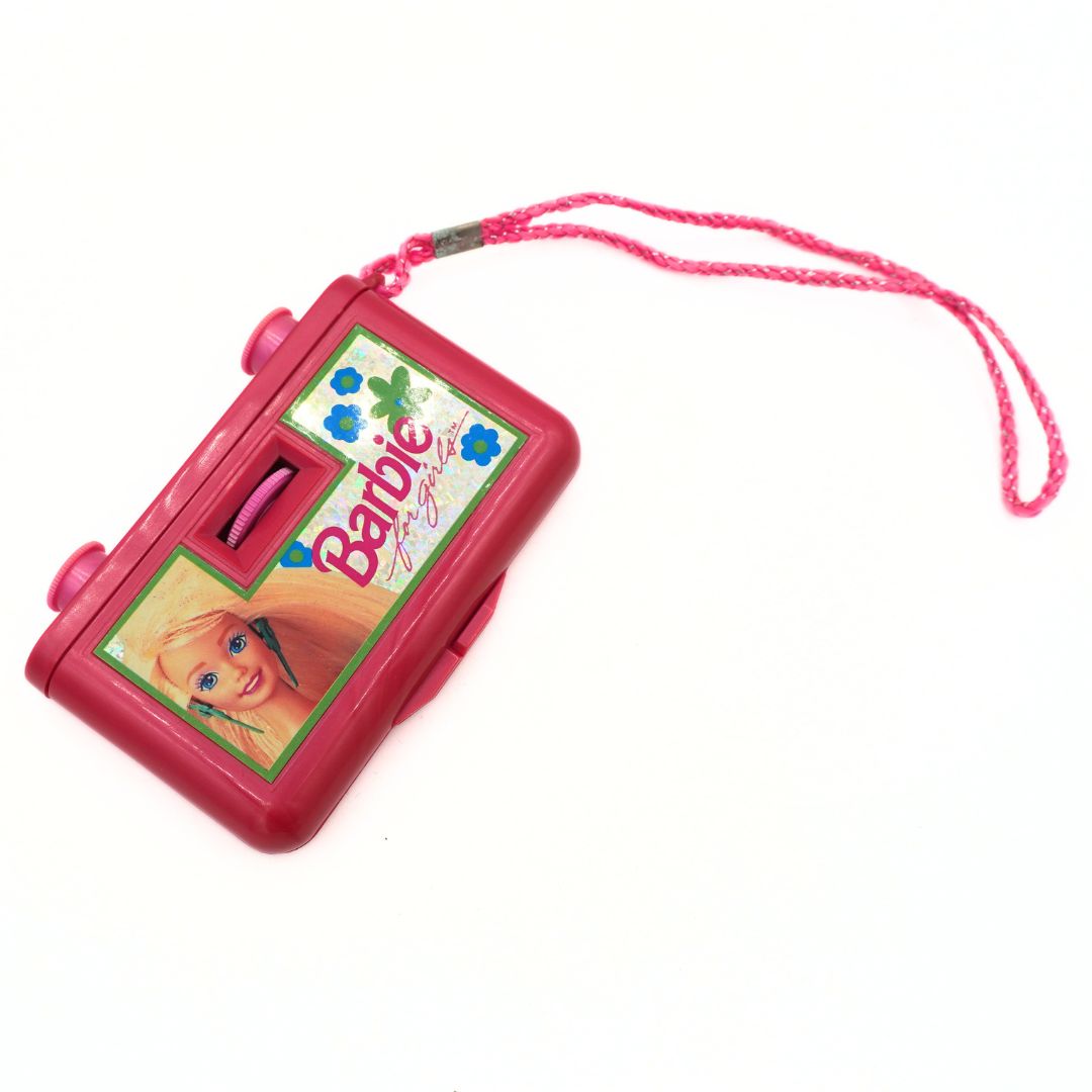 A pink Barbie-themed toy binoculars with a matching pink wrist strap, featuring a printed Barbie logo and illustration on the front, set against a plain white background.
