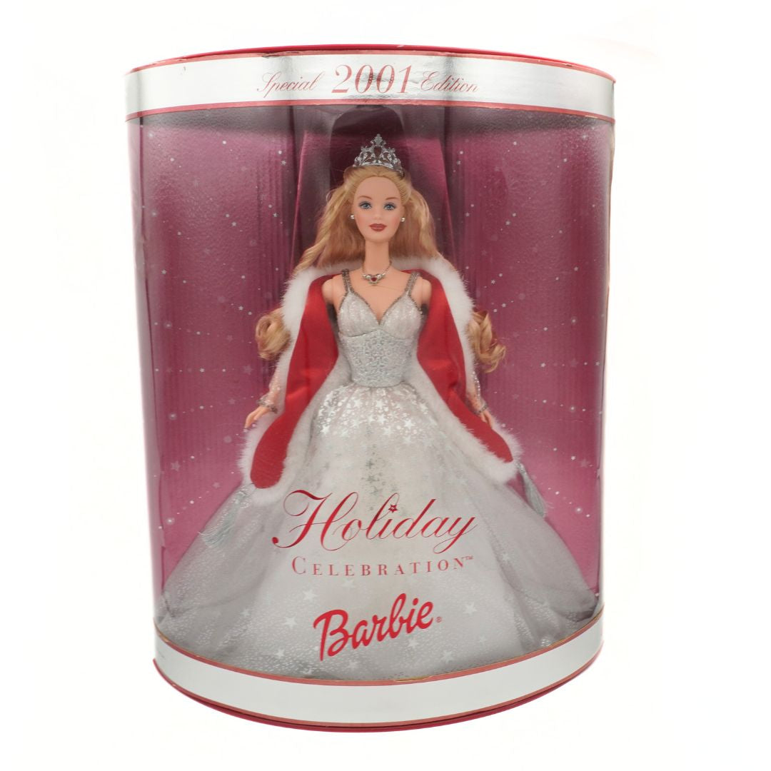 Barbie doll in a holiday dress with red cape in a clear cylindrical box on a white background