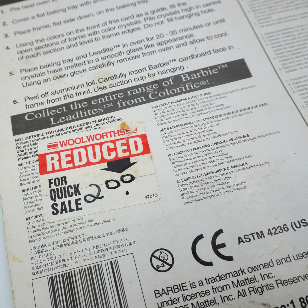Close-up of the back of a Barbie Leadlit's plastic tray packaging insert, showing instructions, warnings, barcodes, and a large red 'REDUCED FOR QUICK SALE' sticker overlay.