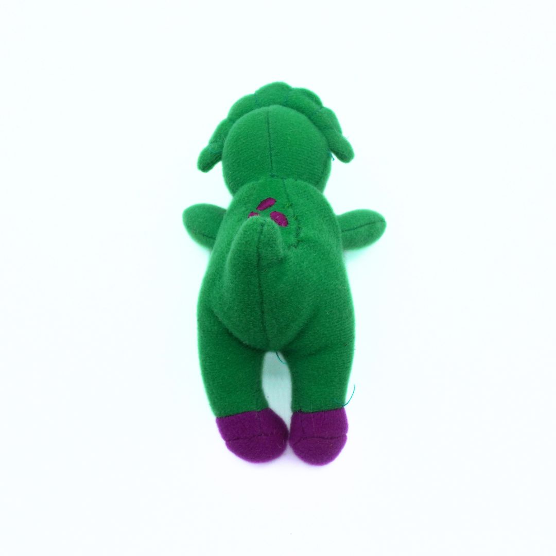 Green plush toy with purple feet on a white background