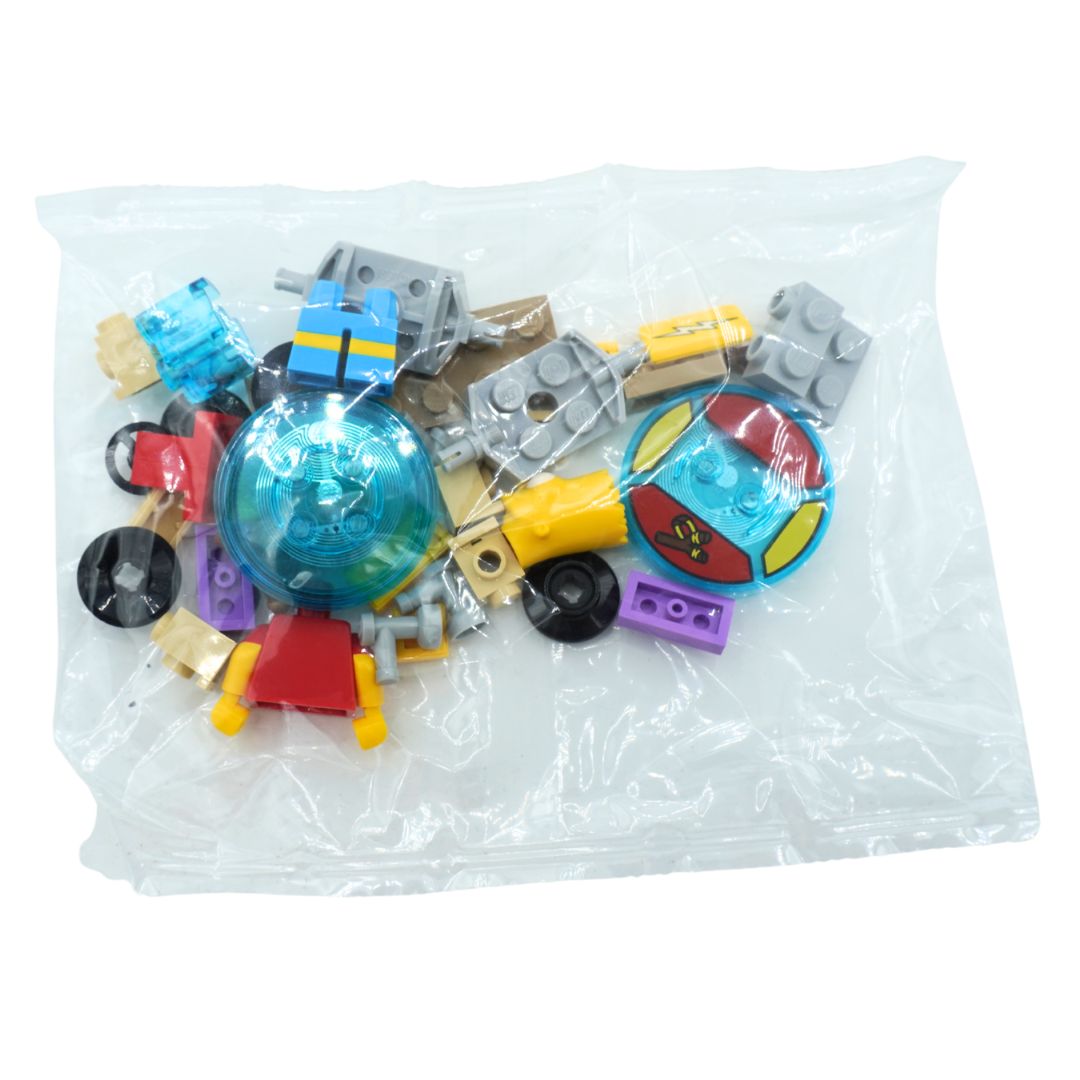 A clear plastic bag containing assorted small toy building-block pieces and accessories, including gray plates, a translucent blue dome, yellow and red pieces, and purple and black wheels, photographed on a white background.