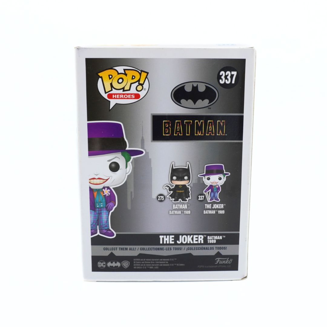 Funko Pop! Heroes Batman The Joker #337 collectible figure in its original window box packaging, featuring the Joker character with a purple suit and hat, black and white face, and red smile.