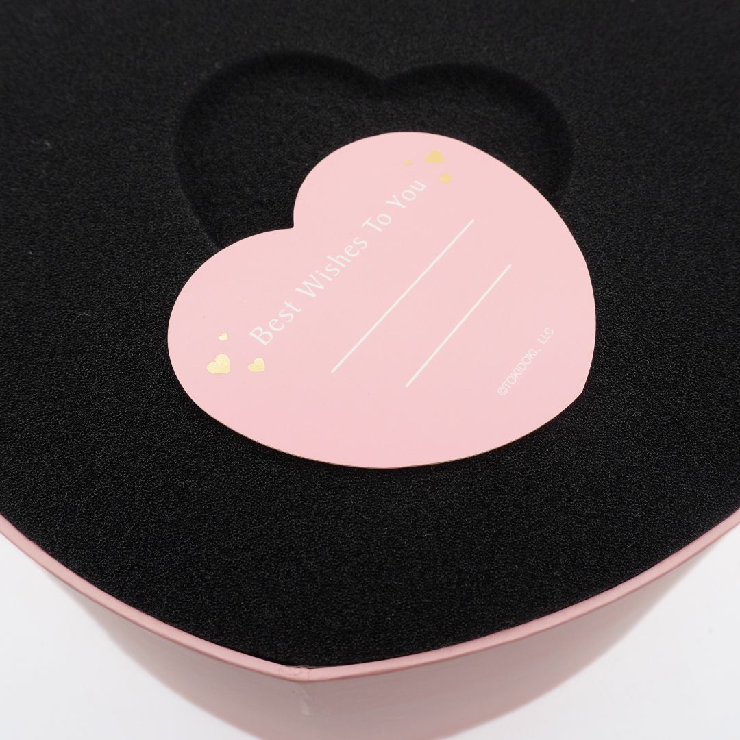 A close-up of a heart-shaped pink gift box interior with black velvet lining and a matching pink heart-shaped insert card that reads 'Best Wishes To You' with small gold heart accents.