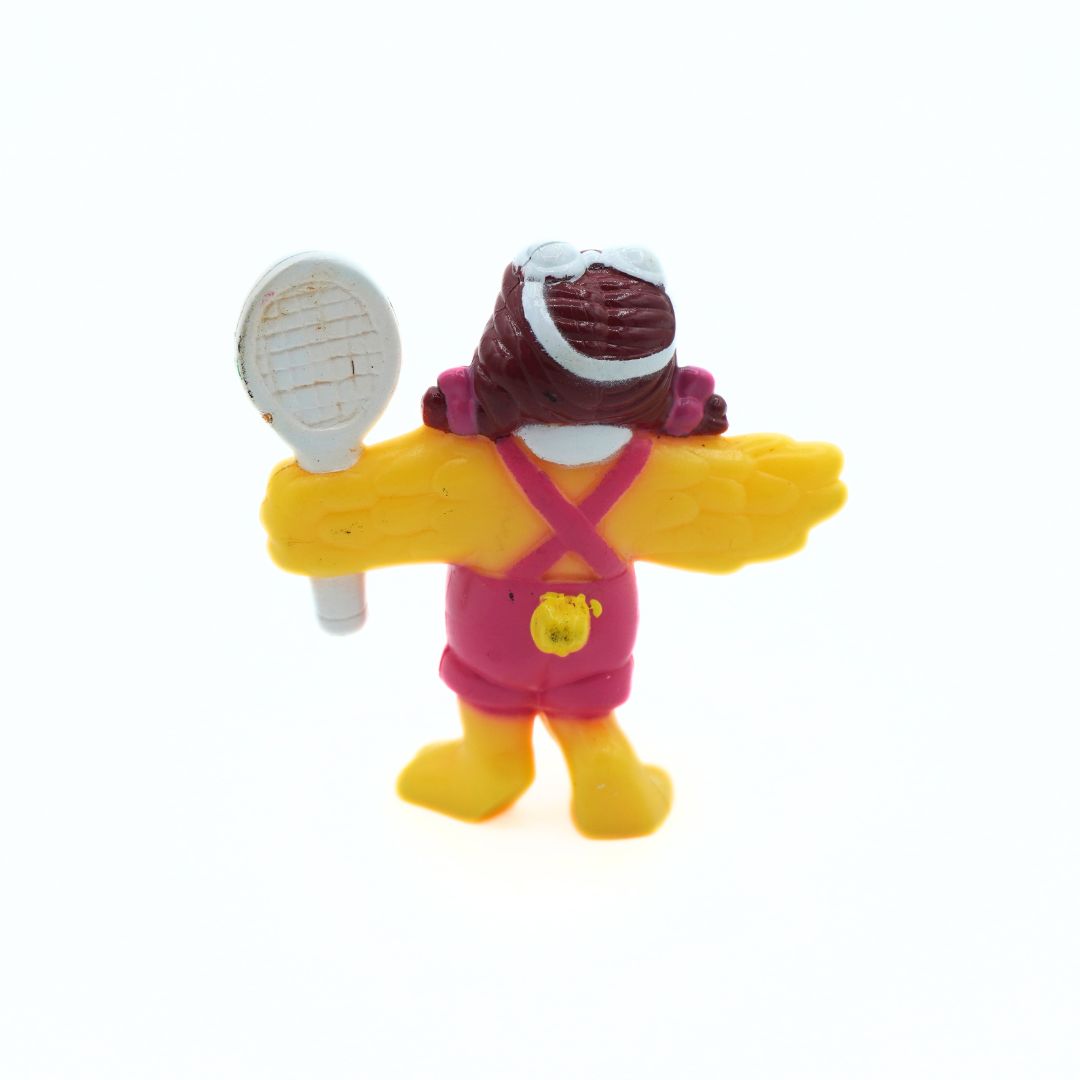 A small plastic toy figure of a bird character seen from the back, wearing pink overalls, yellow boots, and holding a white tennis racket, on a plain white background.