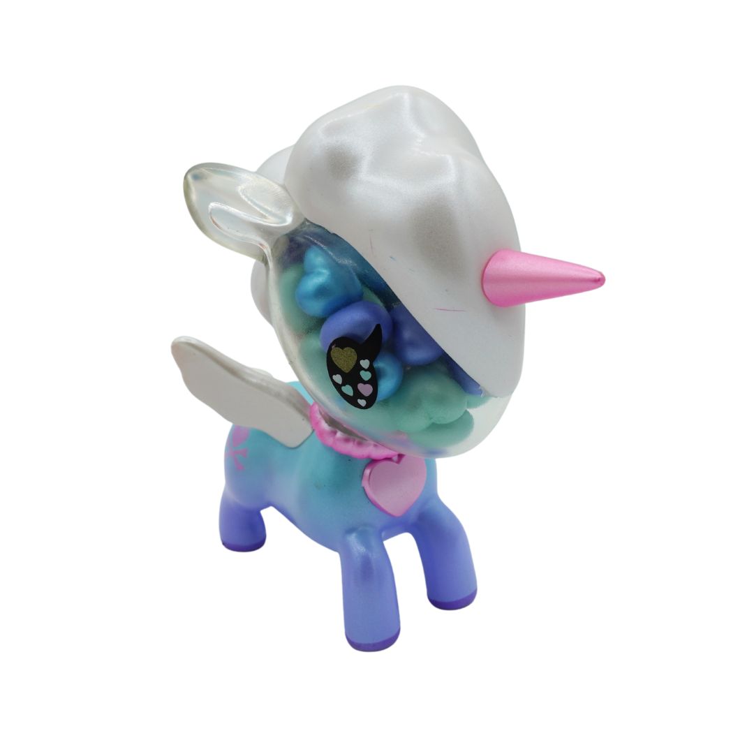 A small stylized unicorn toy figure with a white horn and body, pastel blue and purple legs, translucent wings, and a pink heart-shaped accessory, shown on a plain white background.