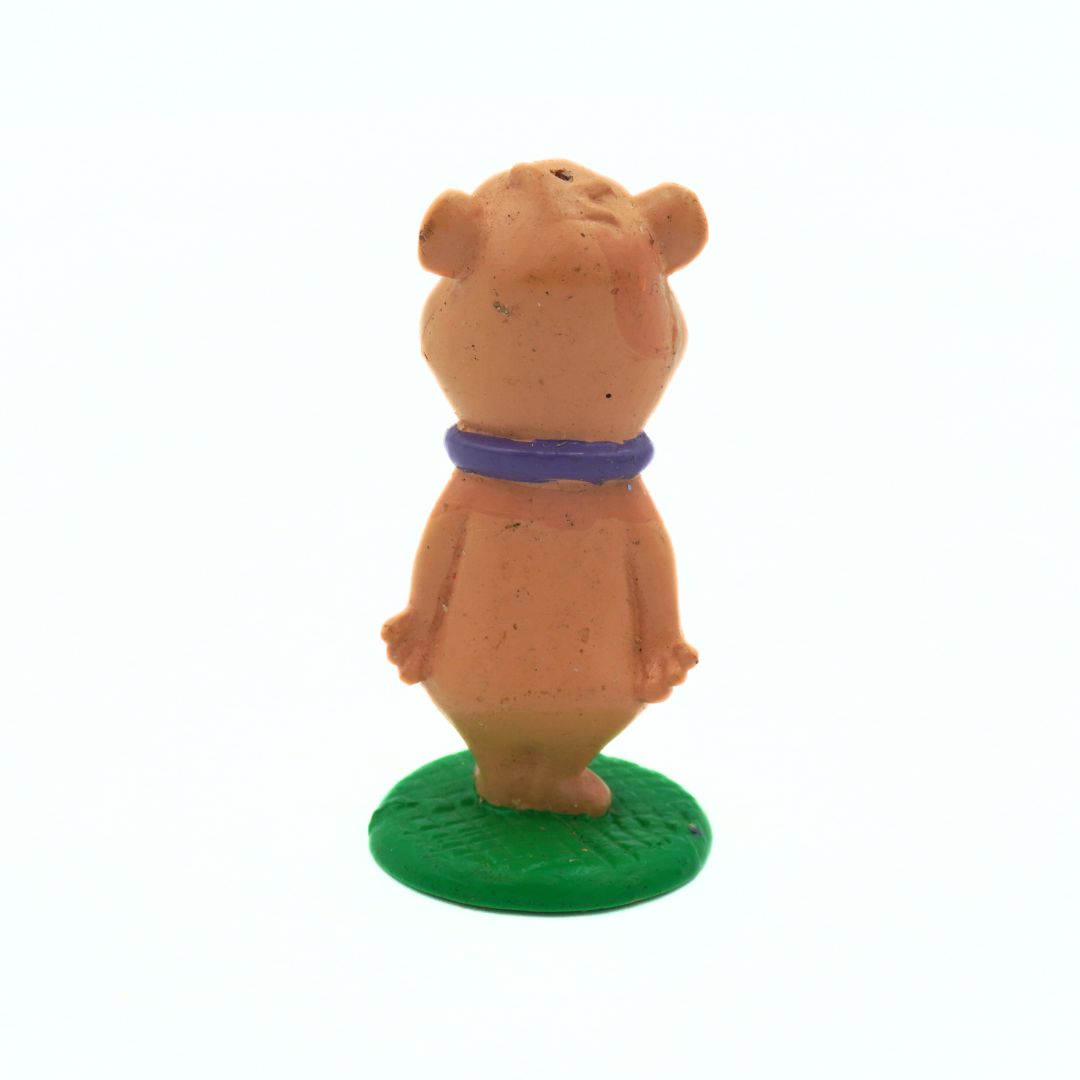 Small figurine of a bear with a purple collar on a green base against a white background