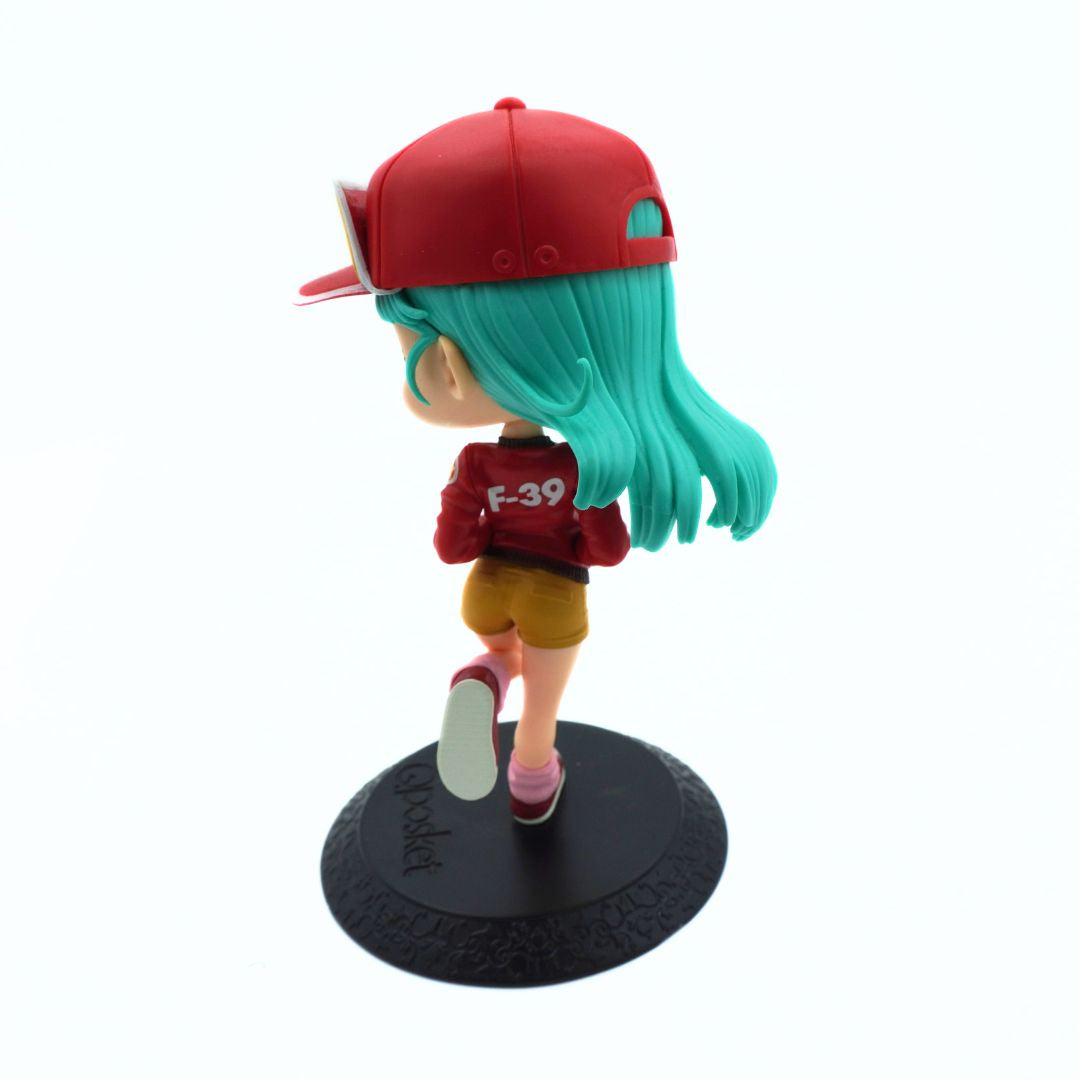A chibi-style anime figurine of a character with long turquoise hair, wearing a red cap, red top, yellow shorts, and pink shoes, standing on a black round display base against a white background.