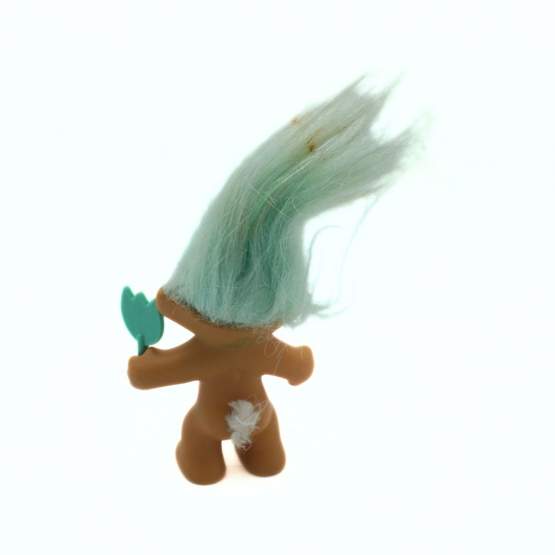 Small figurine with green hair and a leaf on a white background
