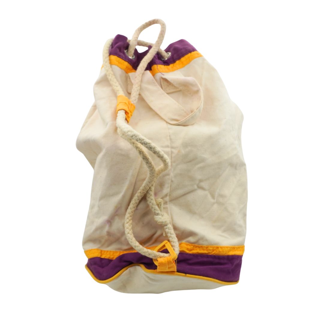 A cream-colored canvas drawstring bag with purple and yellow trim, shown against a plain white background.