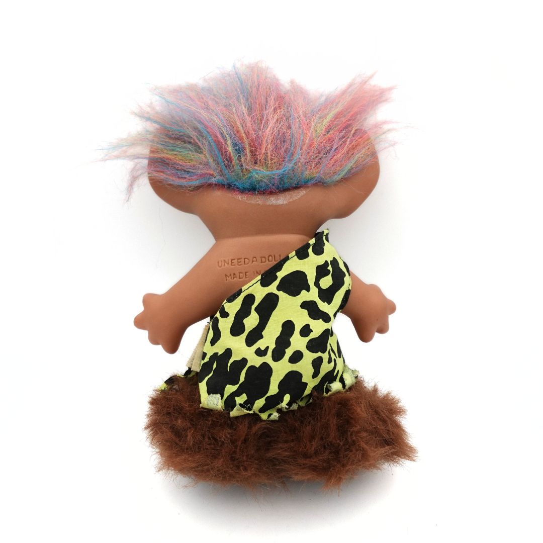 Photo of the back of a Caveman Troll Doll released by Uneeda, with a green and black outfit, brown boots and rainbow hair