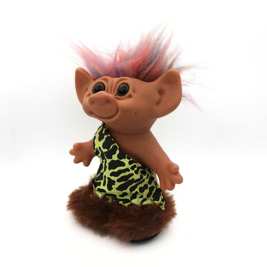 Angled photo of a vintage Caveman Troll Doll released by Uneeda, with a green and black outfit, brown boots and rainbow hair