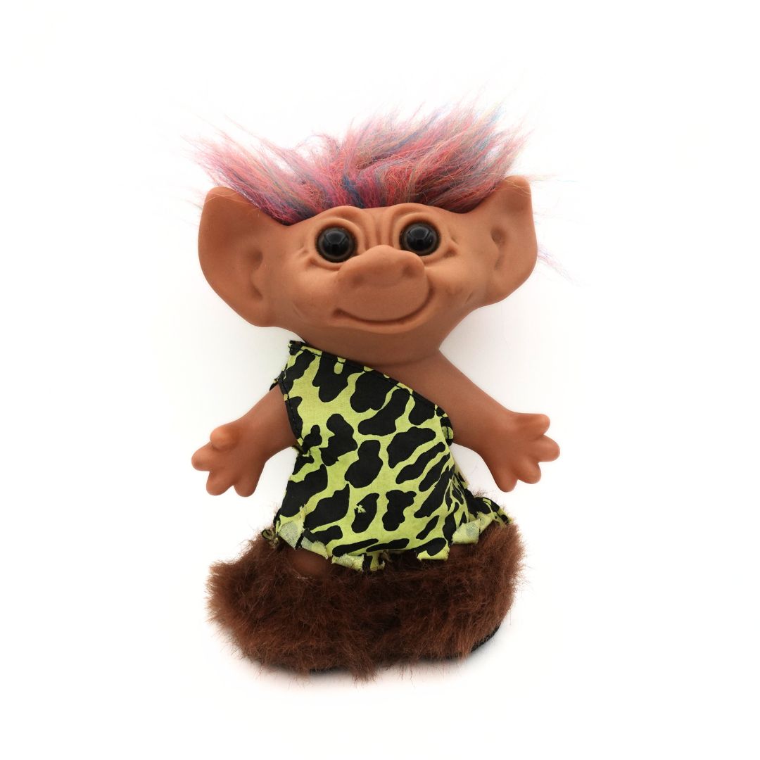 Front on photo of a vintage Caveman Troll Doll released by Uneeda, with a green and black outfit, brown boots and rainbow hair