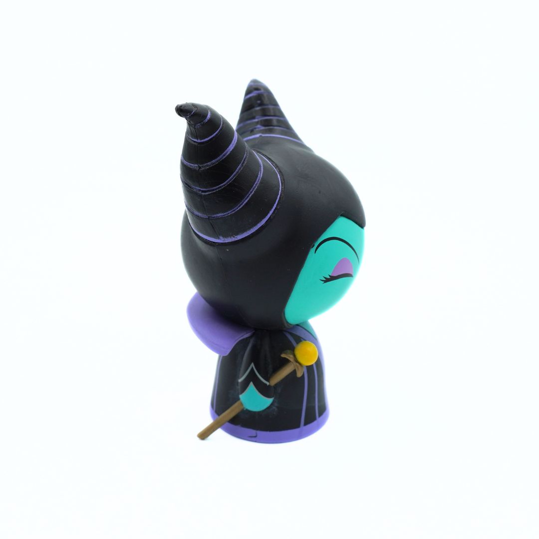A stylized collectible figurine of Maleficent from Disney's Sleeping Beauty, shown from a side-back angle against a solid white background. The figure features her signature black and purple wizard hat and robe, with a bright teal face and a small gold staff.
