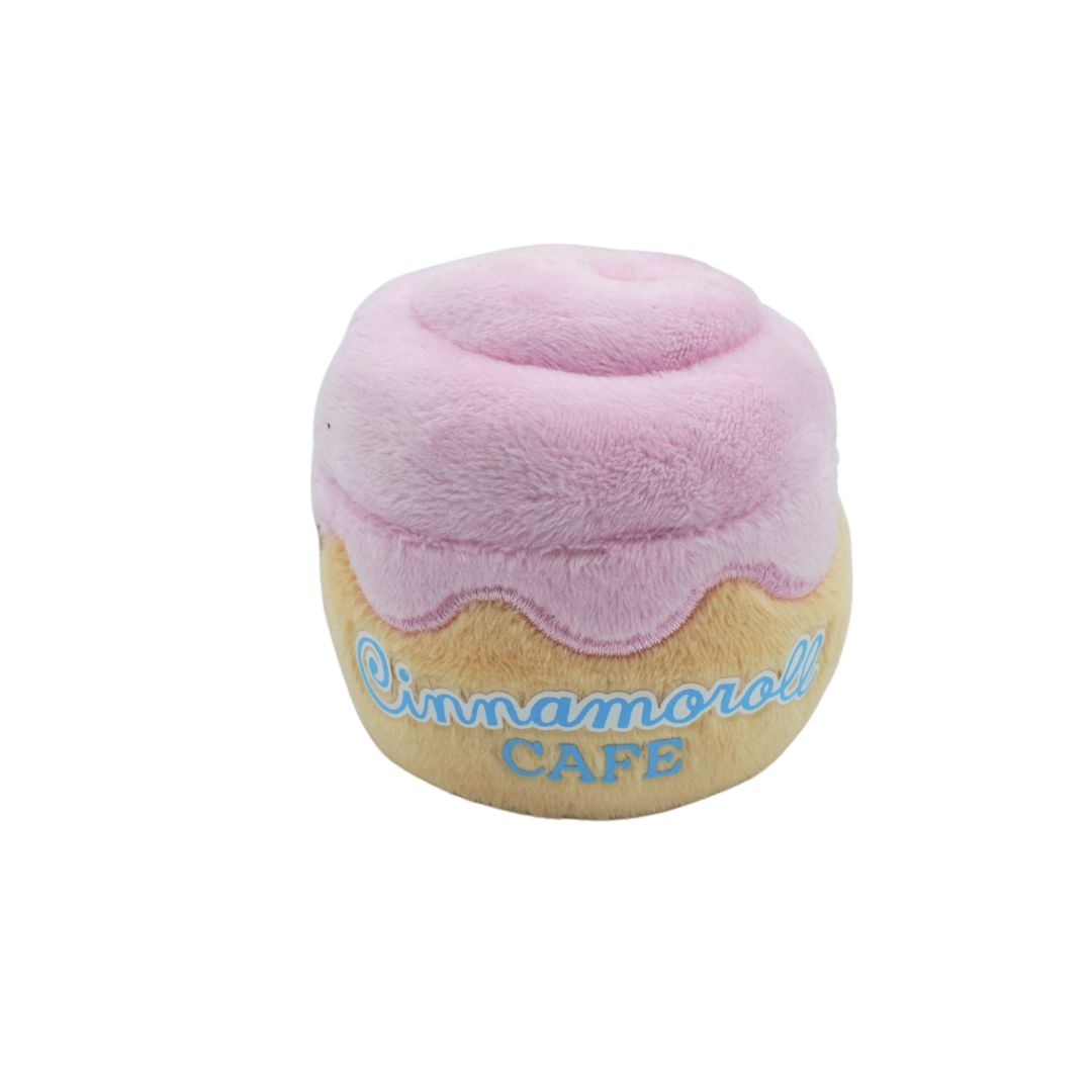 A plush donut-shaped cushion with pink frosting, a beige pastry base, and embroidered blue text reading 'Cinnamoroll CAFE' on a white background.