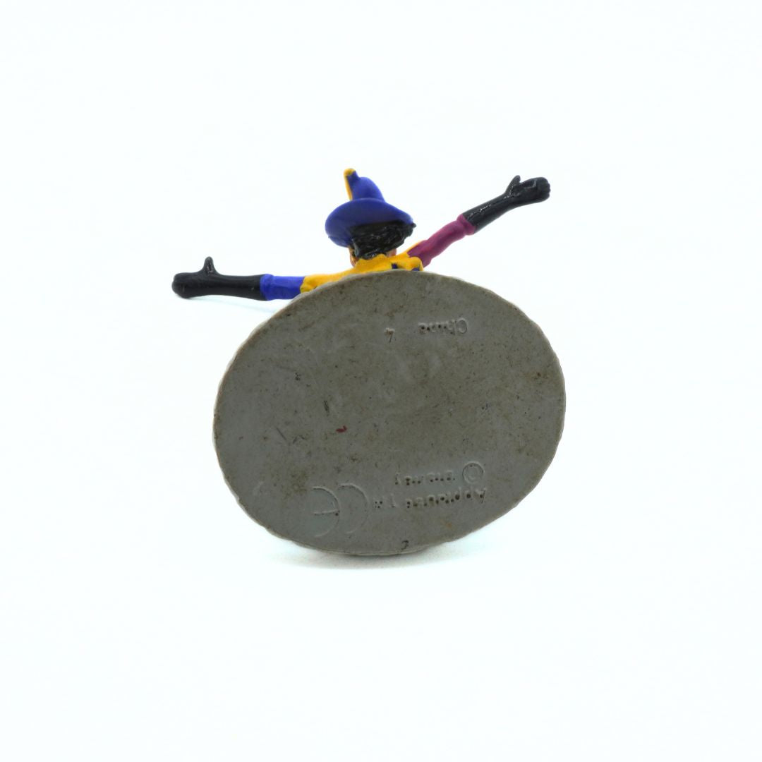 Small figurine of a character with a blue hat and purple outfit on a concrete block.