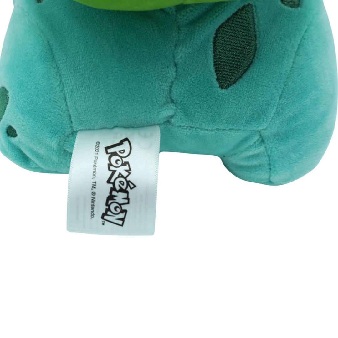Close-up of a teal plush toy with a Pokémon tag on a white background