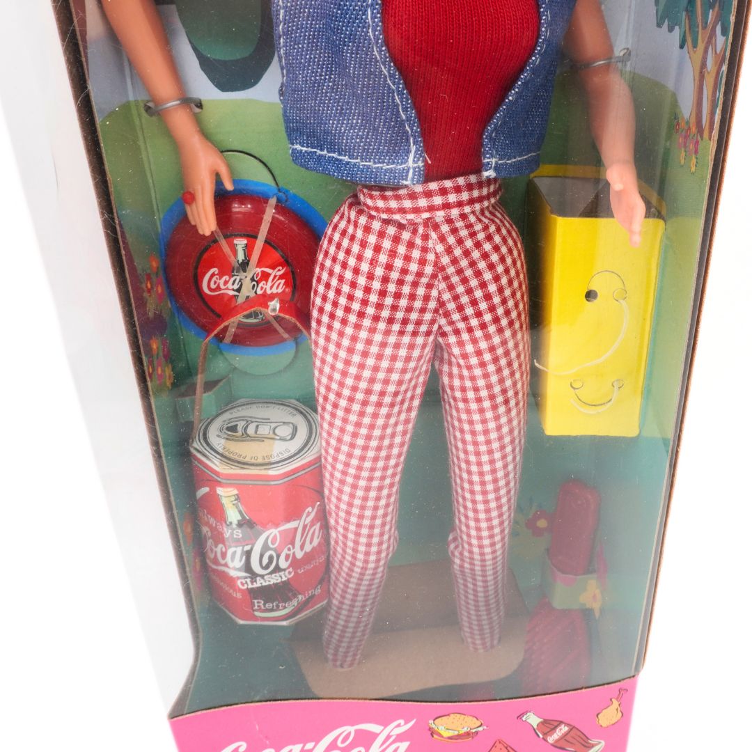 Toy figure in a Coca-Cola branded box with a red and white checkered outfit.