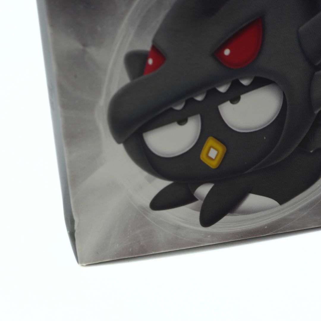 A close-up of a black cartoon monster figure with red eyes and a small yellow square mouth detail, shown inside or against a gray circular insert on a white background.