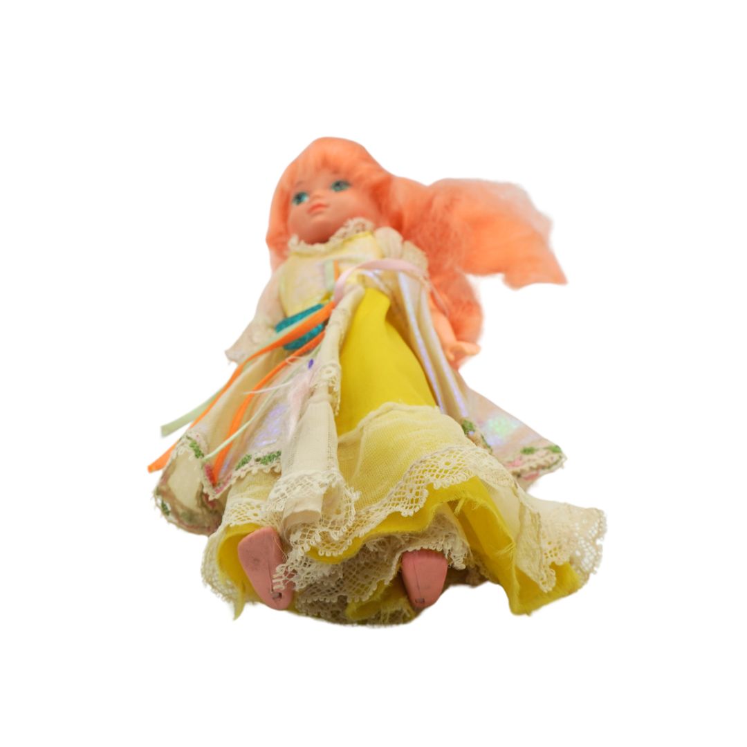 A vintage doll with orange hair and a yellow dress with lace trim, isolated on a white background.