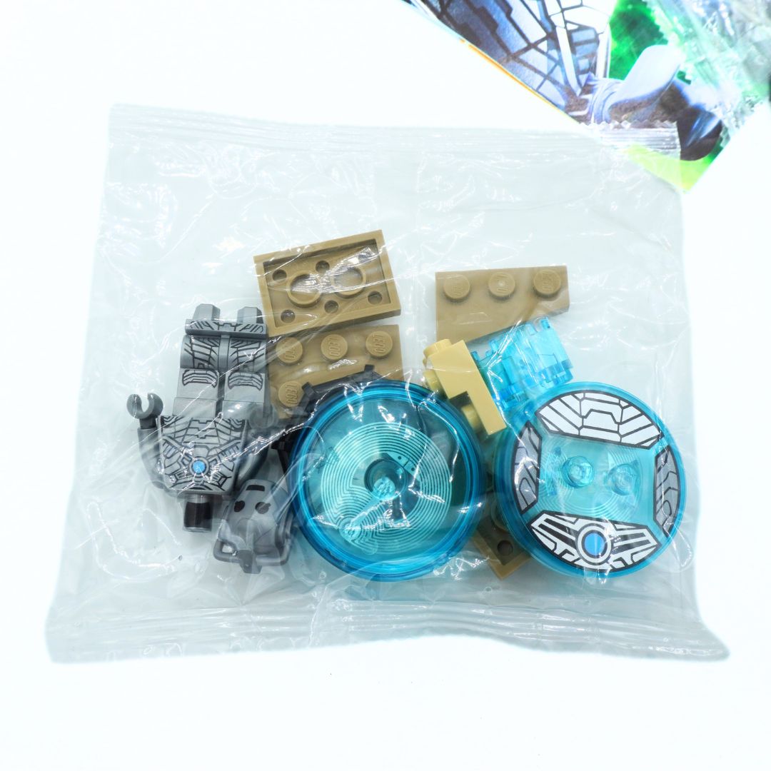A clear plastic bag containing small toy building-block style pieces, including tan rectangular studs, a gray character piece, and translucent blue circular pieces, photographed on a white background.
