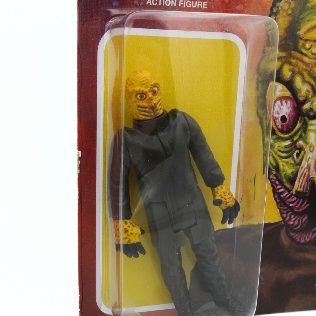 Action figure in packaging with a yellow mask and gray suit on a yellow background