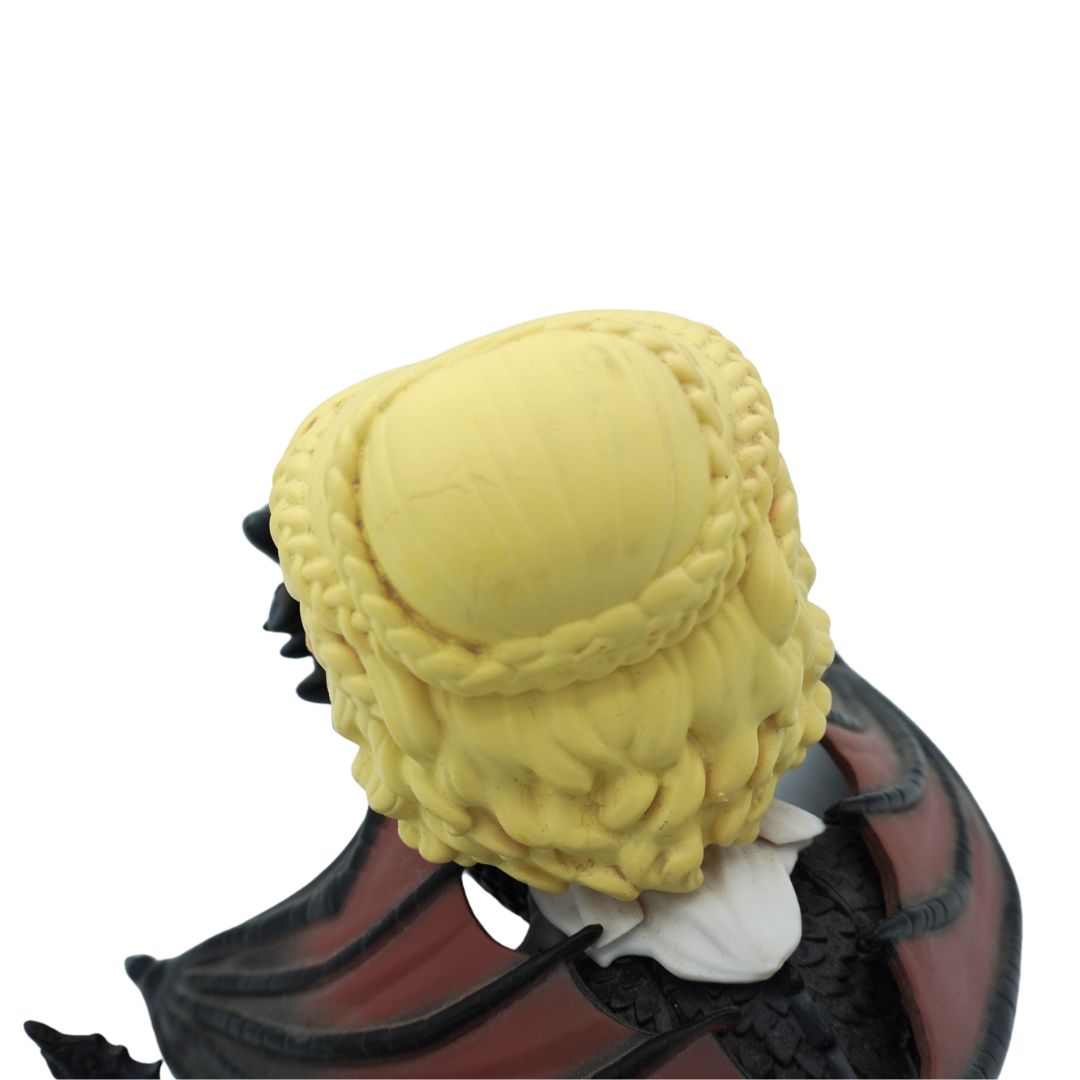 A close-up back view of a collectible figure or bust with long yellow braided hair, a white collar, and dark red and black wings against a plain white background.