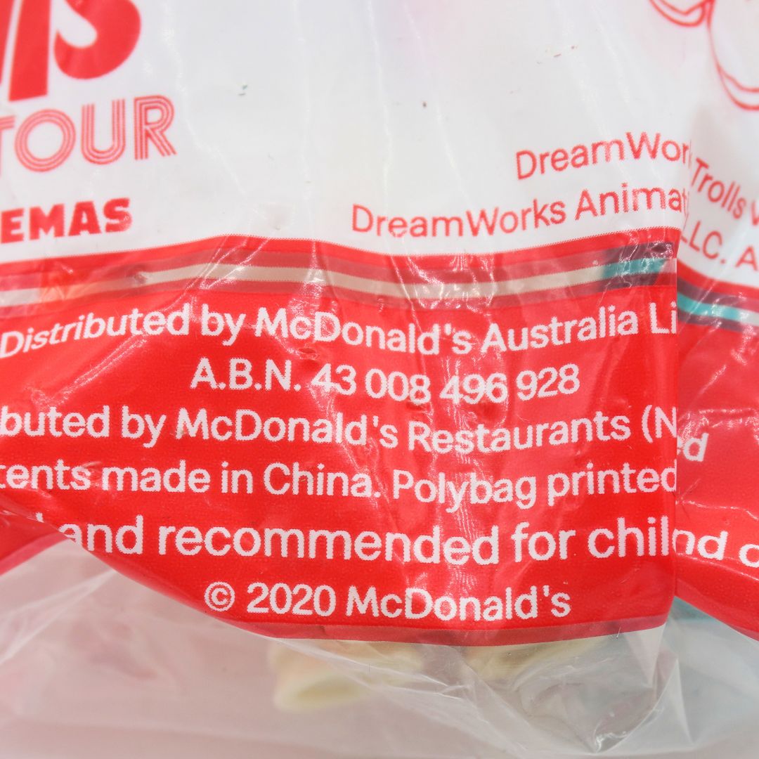Close-up of a McDonald's DreamWorks Trolls themed toy bag, showing printed red and white branding and distribution text on a clear plastic bag.