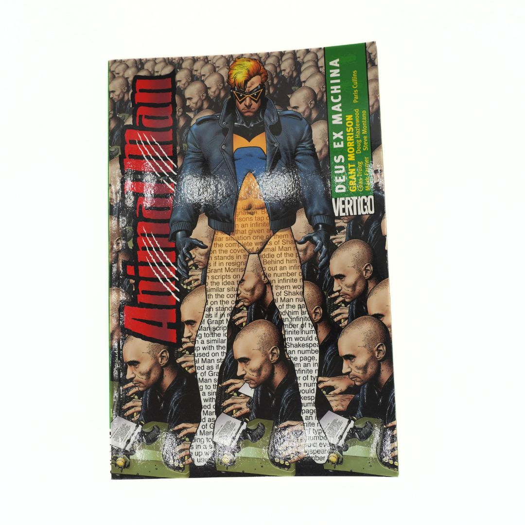 A physical copy of Animal Man Deus Ex Machina by Vertigo, featuring a cover illustrated with a collage of bald men and a central figure in a blue and gold suit. The cover also features a green vertical banner with the text 'DEUS EX MACHINA' and 'VERTIGO'.