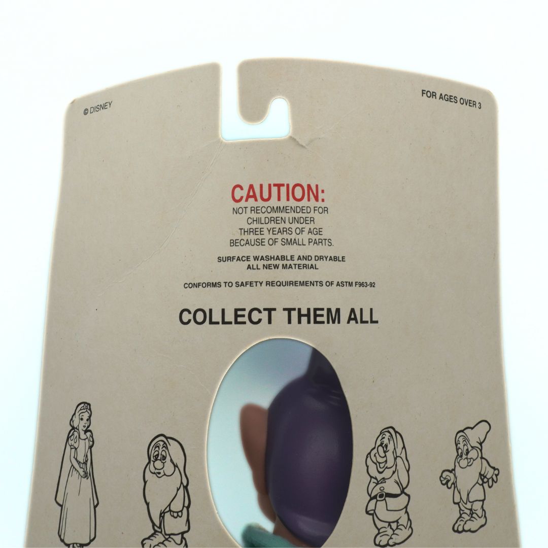 Toy packaging with a purple character inside, featuring Disney branding and safety warnings.