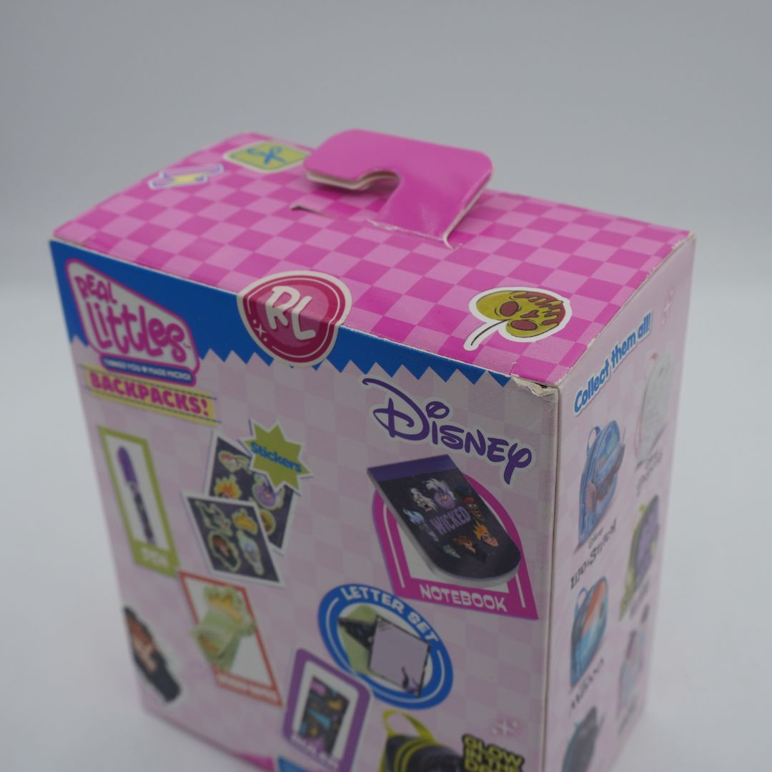 A pink and white checkered Disney 'Real Littles Backpacks!' retail box with a die-cut handle, photographed on a light gray background.